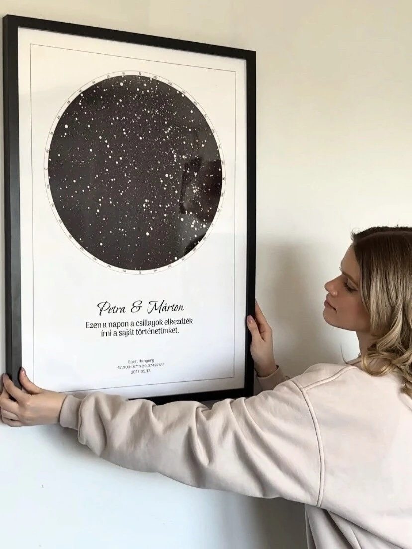 Egy nő egy egyedi nászajándékot akaszt a falra: egy csillagtérkép Petra és Márton esküvőjére.