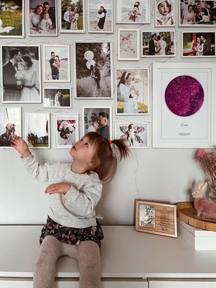 Egy kislány a gyerekszoba falát nézi, ahol egy születési csillagtérkép látható, mint ajándék gyerekeknek.