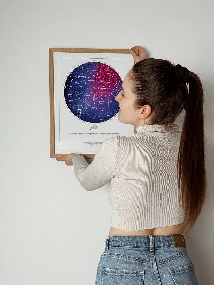 Egy nő egy "Lili" névre szóló születési csillagtérképet akaszt a falra, "A nap, amikor a te történeted elkezdődött" felirattal.
